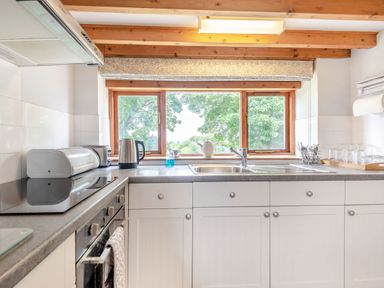 A kitchen with white cabinets a stove kettle sink and utensils on the counter at Tryfan Cottage in Rhostryfan near Caernarfon