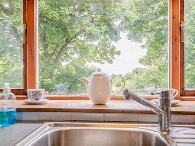 A kitchen sink with a faucet and a windowsill featuring a teapot, two cups and saucers, and a soap dispenser at Tryfan Cottage in Rhostryfan near Caernarfon