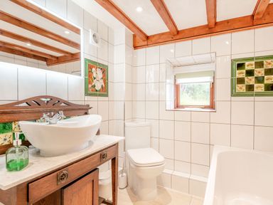 A bathroom with a sink on a wooden vanity a toilet a bathtub and a small window at Tryfan Cottage in Rhostryfan near Caernarfon