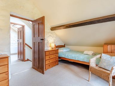 A bedroom with a single bed a wooden chest of drawers a wicker chair and exposed wooden beam at Tryfan Cottage in Rhostryfan near Caernarfon