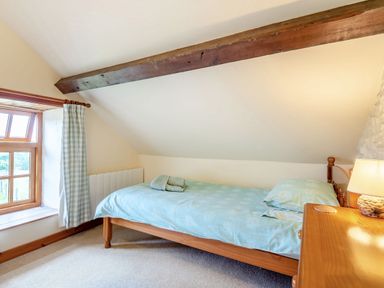 A single bed with blue bedding next to a window and a wooden nightstand with a lamp at Tryfan Cottage in Rhostryfan near Caernarfon