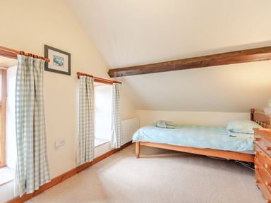 A bedroom with a single bed a wooden dresser two windows with checkered curtains and a framed picture on the wall at Tryfan Cottage in Rhostryfan near Caernarfon