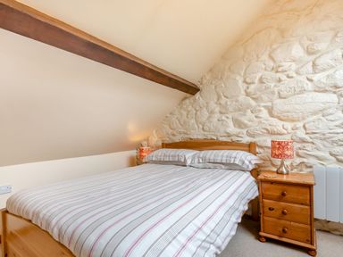 A bedroom with a double bed striped bedding wooden bedside table and stone wall at Tryfan Cottage in Rhostryfan near Caernarfon