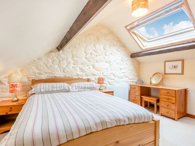 A bedroom with a wooden bed and striped bedding two bedside tables with lamps a wooden dressing table with a mirror a skylight window and stone wall at Tryfan Cottage in Rhostryfan near Caernarfon