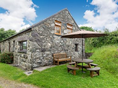 A stone cottage with wooden bench and round picnic table with umbrella on grass at Tryfan Cottage in Rhostryfan near Caernarfon