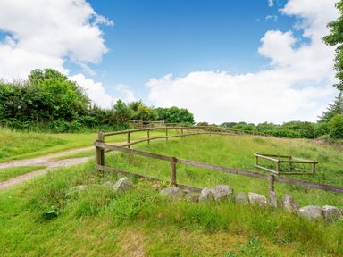 A grassy field enclosed by wooden fences and stone edging under a partly cloudy sky at Tryfan Cottage in Rhostryfan near Caernarfon