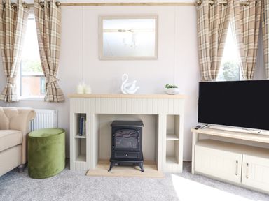 A living room with a fireplace, a television, and windows with plaid curtains at 25 Sherwood in South Lakeland Leisure Village
