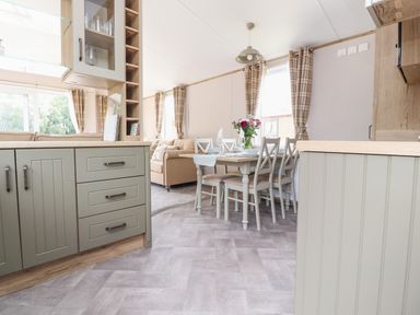 A kitchen with cabinets and a dining table set with chairs and flowers at 25 Sherwood in South Lakeland Leisure Village