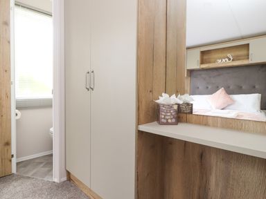A bedroom area with a built-in wardrobe and a mirror reflecting a bed with pillows at 25 Sherwood in South Lakeland Leisure Village