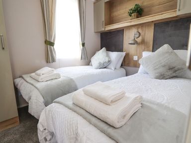 A bedroom with two single beds towels on the beds and a window with curtains at 25 Sherwood South Lakeland Leisure Village