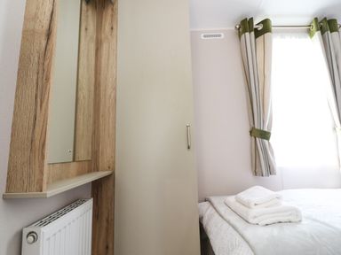A bedroom with a bed with folded towels and a window with green and white curtains at 25 Sherwood in South Lakeland Leisure Village