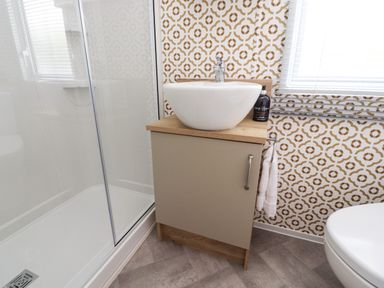 A bathroom with a glass shower enclosure a sink on a wooden cabinet and a toilet at 25 Sherwood in South Lakeland Leisure Village
