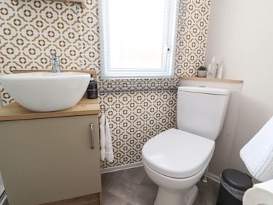 A bathroom with a white sink on a wooden cabinet and a white toilet next to a window with patterned wallpaper at 25 Sherwood South Lakeland Leisure Village