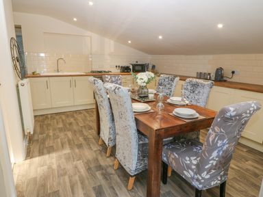 A kitchen with a wooden dining table set with tableware and chairs at The Apartment at Plas Yr Eithin in Amlwch near Llanfechell