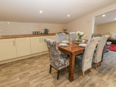 A dining area with a wooden table set for six and light cabinetry at The Apartment at Plas Yr Eithin in Amlwch near Llanfechell