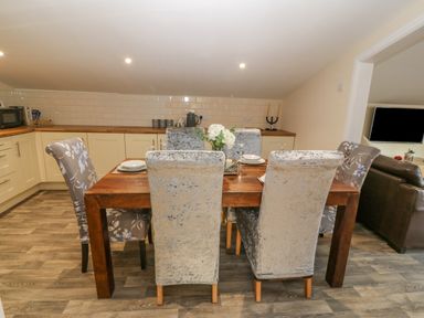 A dining table with six chairs in a kitchen area with cabinets and wooden countertops at The Apartment at Plas Yr Eithin in Amlwch near Llanfechell