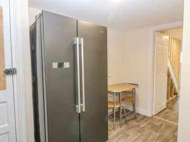 A kitchen area with a large black double door refrigerator and a small wooden table with chairs at The Apartment at Plas Yr Eithin in Amlwch near Llanfechell