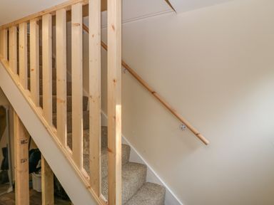 A carpeted staircase with a light wooden handrail and vertical wooden balusters at The Apartment at Plas Yr Eithin in Amlwch near Llanfechell