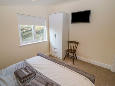 A bedroom with a bed a white wardrobe a wooden chair and a wall mounted tv at The Apartment at Plas Yr Eithin Amlwch near Llanfechell