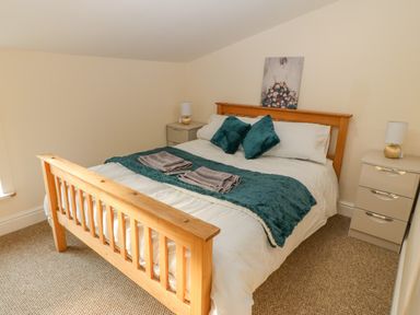 A bedroom with a wooden bed frame two side tables with lamps and folded towels on the bed at The Apartment at Plas Yr Eithin in Amlwch near Llanfechell