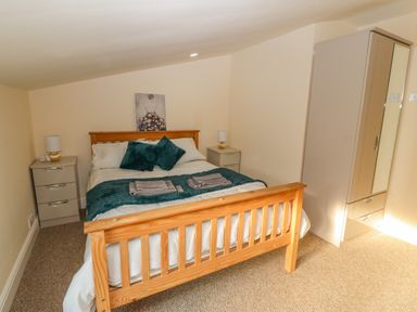 A bedroom with a wooden bed frame two bedside tables with lamps a wardrobe and a painting on the wall at The Apartment at Plas Yr Eithin Amlwch near Llanfechell