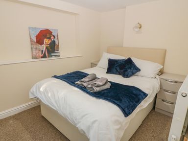 A bedroom with a bed with white bedding and blue pillows and throw with towels on top at The Apartment at Plas Yr Eithin Amlwch near Llanfechell