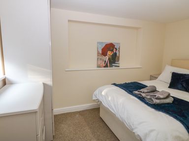 A bedroom with a bed covered with white and blue bedding and a painting of a couple with an umbrella on a shelf at The Apartment at Plas Yr Eithin Amlwch near Llanfechell