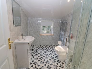 A bathroom with a sink, mirror, toilet, glass shower enclosure, towel radiator, and window at The Apartment at Plas Yr Eithin in Amlwch near Llanfechell