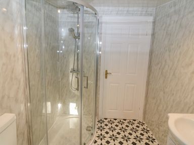 A bathroom with a glass shower enclosure a white door a toilet and a sink with patterned floor tiles at The Apartment at Plas Yr Eithin in Amlwch near Llanfechell