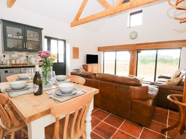 An open plan kitchen dining and living area with wooden table and chairs leather sofas and large sliding glass doors at Little Barn in Tittleshall