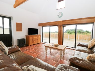 A living room with leather sofas a wooden coffee table a TV on a wooden cabinet and large windows at Little Barn in Tittleshall