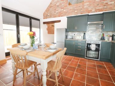 A kitchen with wooden dining table and chairs and green cabinets at Little Barn in Tittleshall