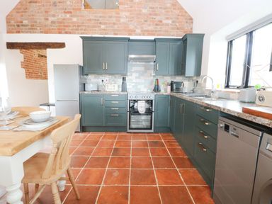 A kitchen with green cabinets terracotta tiled floor a refrigerator oven and a wooden dining table with chairs at Little Barn in Tittleshall