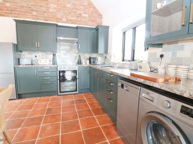 A kitchen with green cabinets oven dishwasher washing machine and tiled floor at Little Barn in Tittleshall