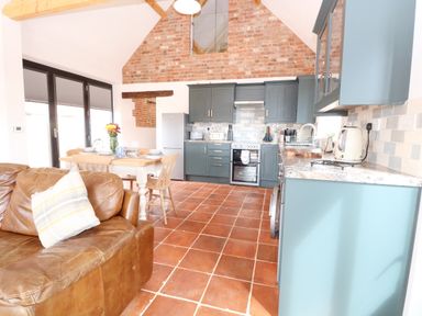 A kitchen with blue cabinets a dining table with chairs and a brown leather sofa at Little Barn in Tittleshall