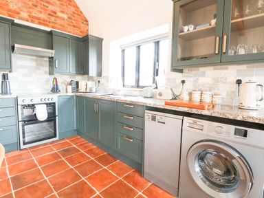 A kitchen with green cabinets a black oven a dishwasher a washing machine and terracotta tiled floor at Little Barn in Tittleshall