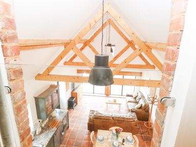 An open living space with exposed wooden beams a dining table with dishes two brown sofas and kitchen cabinets at Little Barn in Tittleshall