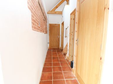 A hallway with terracotta floor tiles exposed brick on one wall wooden doors and beams at Little Barn in Tittleshall