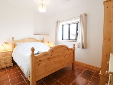 A bedroom with a wooden bed a bedside table with lamps a window with curtains and a wardrobe at Little Barn in Tittleshall