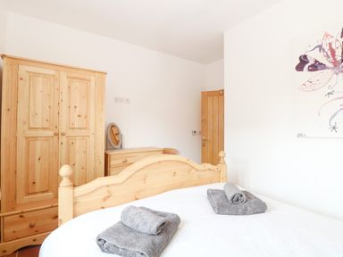 A bedroom with a wooden bed frame gray towels a wooden wardrobe and a dresser with a mirror at Little Barn in Tittleshall