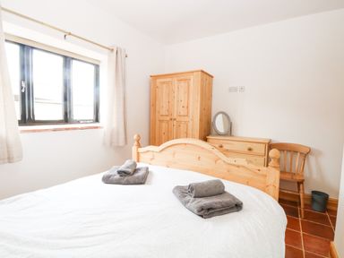 A bedroom with a wooden bed and dresser with a mirror next to a wooden chair and window at Little Barn in Tittleshall