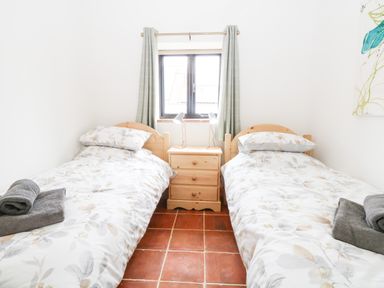 A bedroom with two single beds a wooden nightstand and a window with curtains at Little Barn in Tittleshall
