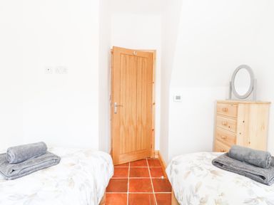 A bedroom with two single beds with gray towels on them a wooden door and a wooden dresser with a round mirror at Little Barn in Tittleshall