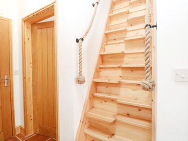 A wooden staircase with rope handrails next to two wooden doors with silver handles at Little Barn in Tittleshall