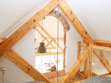 A view of a living room with wooden beams and glass panels from an upper floor at Little Barn in Tittleshall