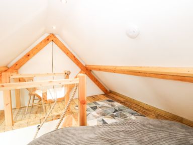 A loft space with wooden beams a chair a small table and a rug at Little Barn in Tittleshall