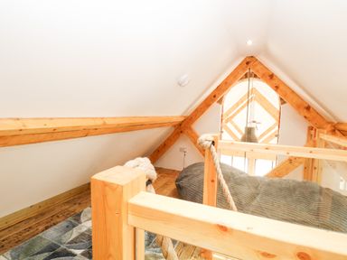 An attic space with wooden beams and railing a gray bean bag and a patterned rug at Little Barn in Tittleshall