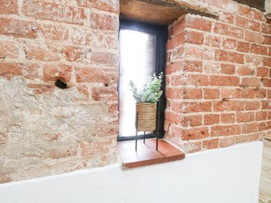 A small window in a brick wall with a potted plant on the windowsill at Little Barn in Tittleshall