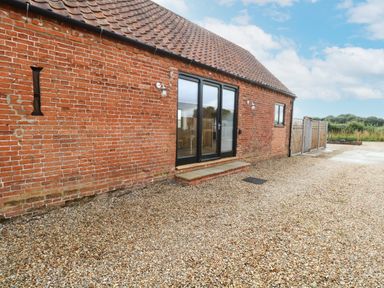 A brick building with a tiled roof a set of glass double doors and gravel ground at Little Barn in Tittleshall