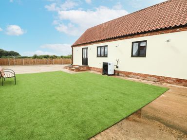 An outdoor area with artificial grass a bench and a building with tiled roof and cream walls at Little Barn in Tittleshall